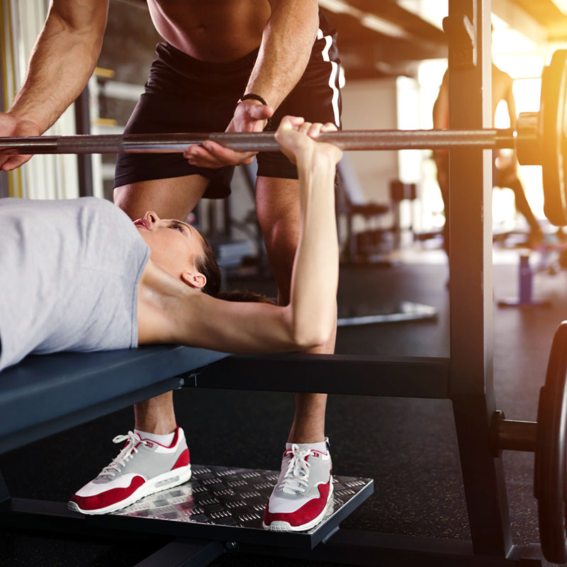 Woman doing a bench press with a personal trainer spotting her during a one on one training session.